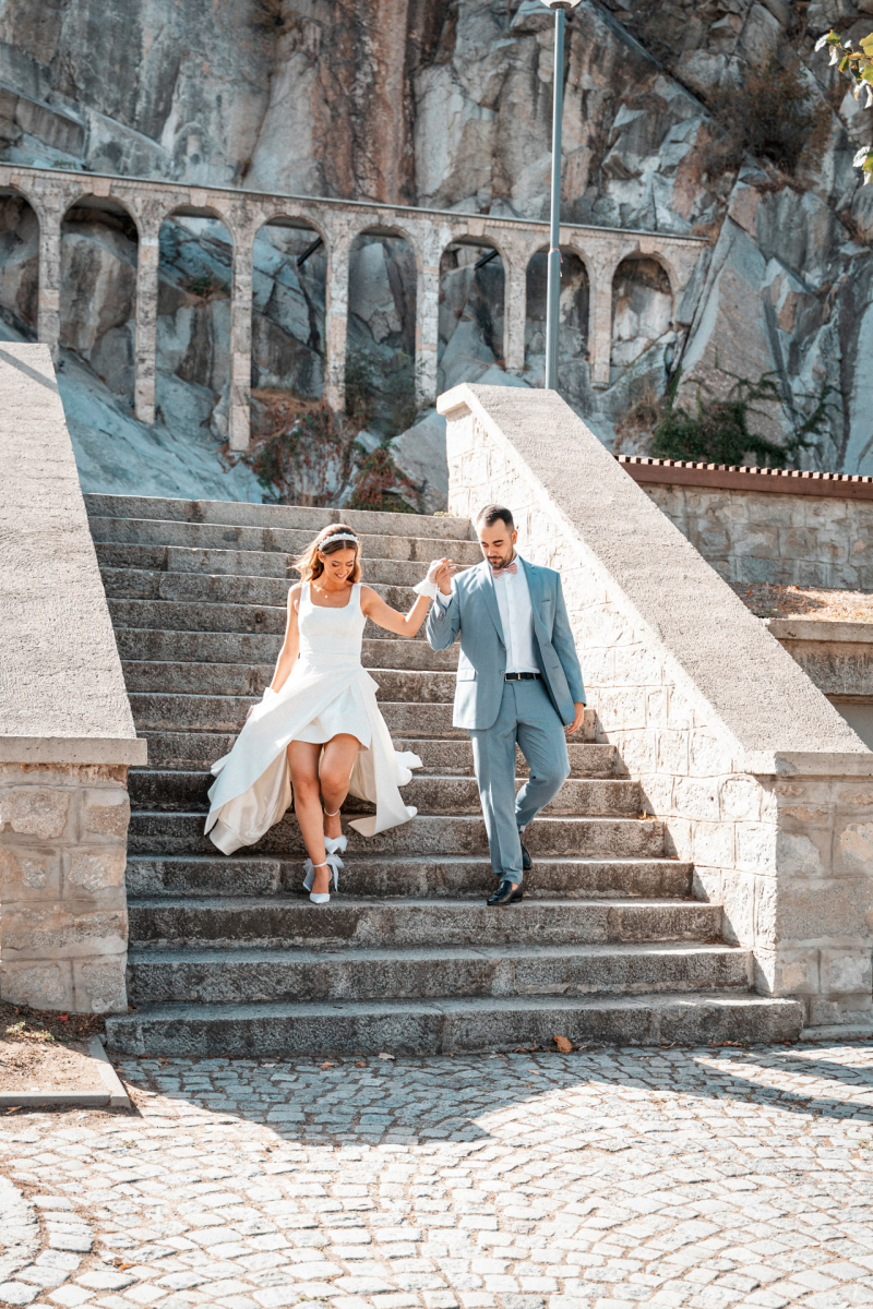 Младоженци слизат по каменни стълби на фона на старинна архитектура | Bride and groom walking down stone stairs against a backdrop of ancient architecture