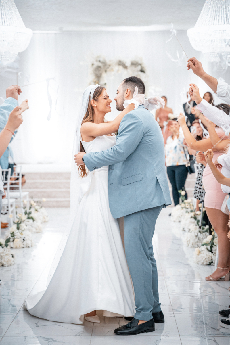 Младоженци се прегръщат по време на граждански ритуал в светла зала | Bride and groom embracing during a civil wedding ceremony in a bright hall