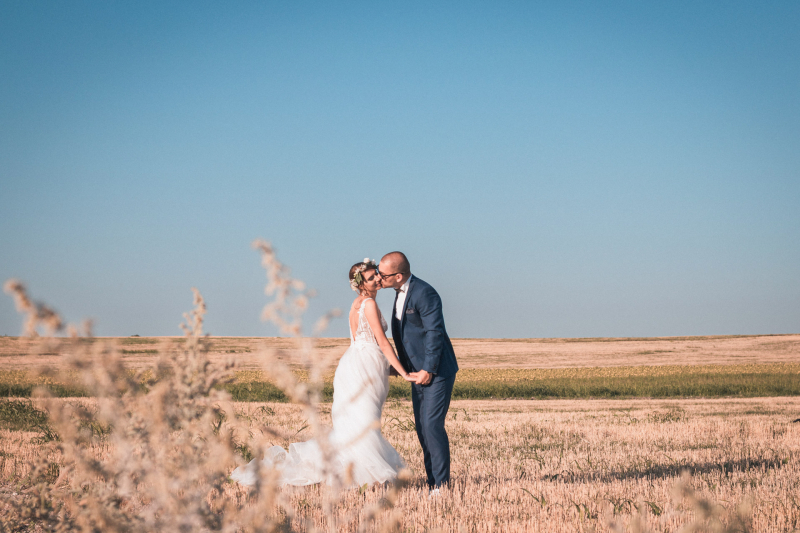 Младоженци се целуват в голямо ожънато поле под синьо небе | Newlyweds kissing in a large harvested field under a blue sky